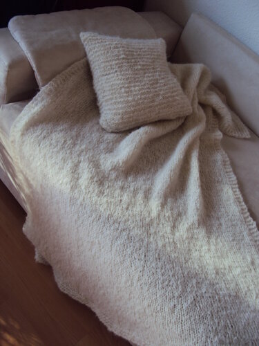 Cremefarbene Strickdecke und passendes Kissen auf hellem Sofa