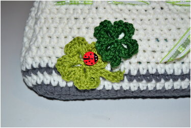 Gehäkelte Tasche in Weiß und Grau mit grünen Kleeblättern und rotem Marienkäfer-Knopf.