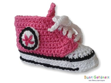 Gehäkelter Babysneaker pink und weiß mit schwarzem Zierstreifen und Kreis-Emblem
