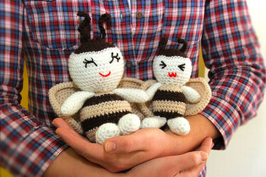 Zwei detailreich gehäkelte Amigurumi-Bienen mit Streifen und Flügeln, in den Händen einer Person.