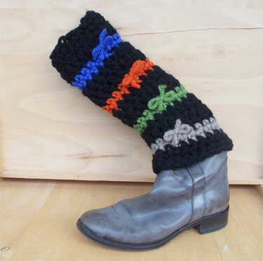 Schwarze gehäkelte Beinstulpe mit bunten Querstreifen über einem grauen Stiefel