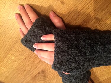 Dunkelgraue gestrickte fingerlose Stulpen mit Strukturmuster an Händen auf Holzoberfläche