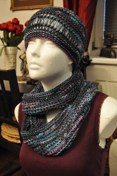 Schaufensterpuppe mit gestricktem Mützen- und Loop-Schal-Set in dunklem Grau mit rosa- und türkisfarbenen Akzenten.