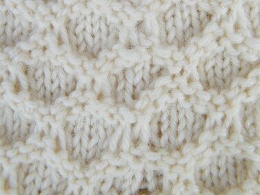 Eng gestricktes cremefarbenes Muster mit klar definierten Maschen.