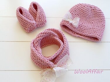 Rosa gestricktes Baby-Set mit Mütze, Babyschühchen und Schlauchschal, mit feinen Schleifen, auf hellem Hintergrund