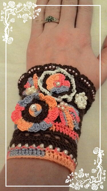 Gehäkeltes braunes Armband mit mehrfarbigen Blumen und Perlen am Handgelenk.