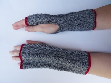 Zwei Arme mit grau gestrickten Armstulpen mit Zopfmuster und rotem Saum