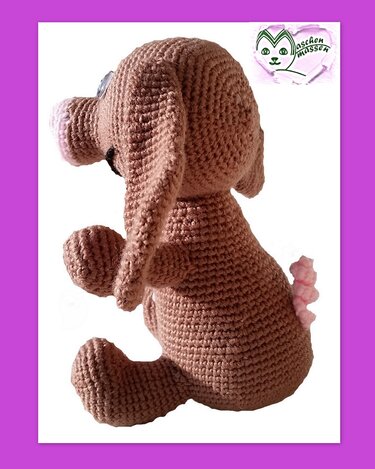 Brauner gehäkelter Amigurumi-Welpe mit rosa Schnauze und Schwanz, seitlich sitzend
