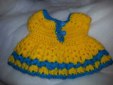 Gelbes gehäkeltes Puppenkleid mit blauen Zierstreifen und zwei Knöpfen