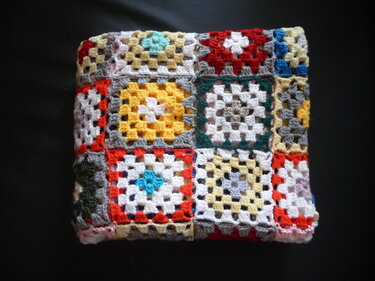 Gefaltete gehäkelte Decke aus bunten Granny-Squares auf dunklem Hintergrund
