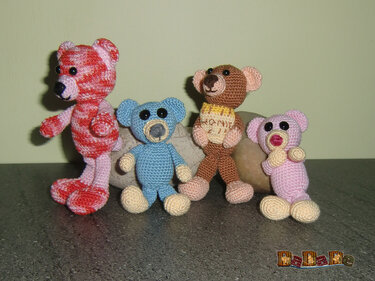 Handmade crochet dolls of four different babies. One with a pink and red striped shirt, one with a blue shirt, one with a brown and yellow striped shirt, and the baby has a cream-colored shirt.