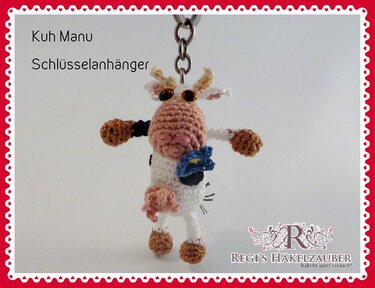Kleiner gehäkelter Amigurumi Kuh-Schlüsselanhänger mit Metallring und blauem Blümchen