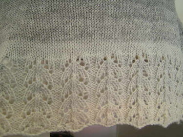 Detail: gestrickter Stoff mit hellgrauem zu weißem Farbverlauf und Blatt-Lochbordüre am Saum