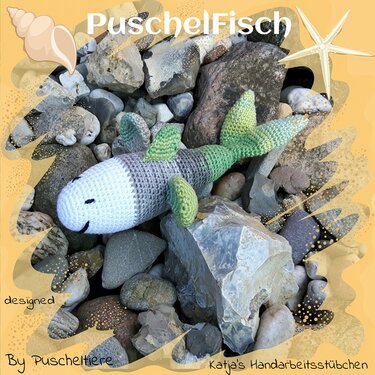 Gehäkelter Amigurumi-Fisch in Grün und Grau auf Kieselsteinen