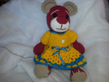 Sitzender gehäkelter Amigurumi-Teddybär rot-beige mit gelbem Kleid und blauen Zierborten