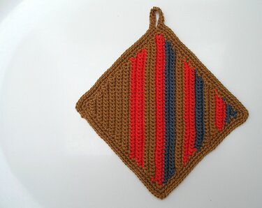 Gehäkelter quadratischer Topflappen in Braun mit roten und blauen Streifen und Aufhängeschlaufe auf weißem Hintergrund.