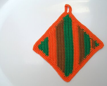 Gehäkelter quadratischer Topflappen orange mit grünen und braunen Streifen und Aufhängeschlaufe auf weißem Hintergrund
