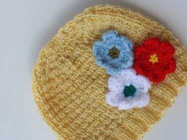 Gelbe Babymütze mit Rippenmuster und drei gehäkelten Blumen (blau, rot, weiß)