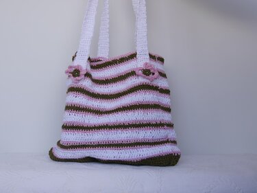 Gehäkelte Umhängetasche mit weiß-rosa-olivgrünen Streifen und Blumenapplikationen