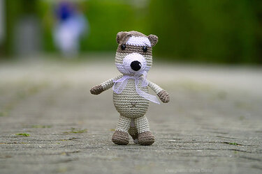 Gehäkeltes Amigurumi-Tier in Beige und Braun mit dunkler Maske und Schleife am Hals