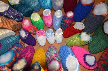 Verschiedene gehäkelte Hausschuhe und Babyschuhe in bunten Farben auf Holzhintergrund.