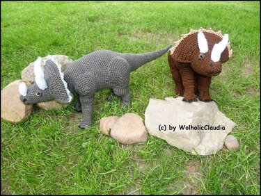 Zwei gehäkelte Triceratops in Grau und Braun auf Gras mit Steinen