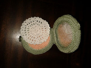 Gehäkelte grüne Spiel-Puderdose, geöffnet, mit weißem Häkeldeckchen und pfirsichfarbenem Innenraum