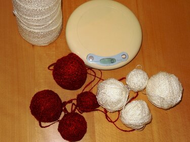 Rote und weiße Garnknäuel, eine Garnspule und eine digitale Waage auf einem Holztisch.