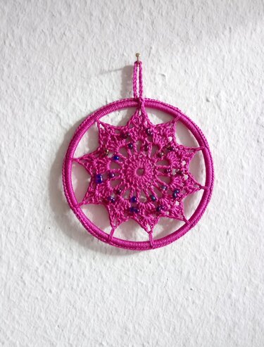 Gehäkelter Stern in Fuchsia mit Perlen an weißer Wand