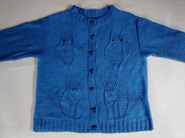 Blaue Kinderstrickjacke mit Knopfleiste, eingestrickten Eulen auf Brusthöhe und Füchsen am Vorderteil.