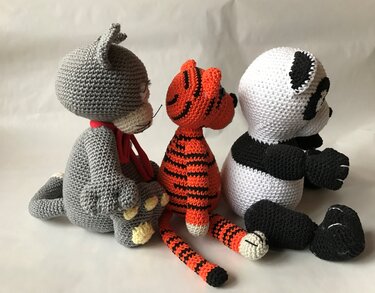 Drei gehäkelte Amigurumi-Tiere (graue Katze, gestreifter Tiger, Panda) in Sitzposition, Seitenansicht