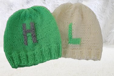 Zwei gestrickte Babymützen für Babys, grün mit grauem H und creme mit grünem L