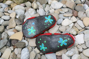 Zwei dunkle Filzstücke mit blauen Blumenmotiven und grünen Tupfen, rot umrandet, auf Flusskieseln.