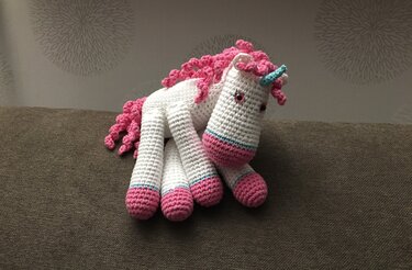 Abbildung eines gehäkelten Einhorn-Amigurumis mit rosa Hufen, weißem Körper und türkisfarbenem Horn