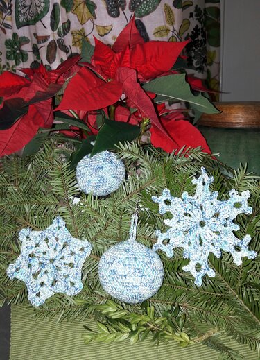 Handgehäkelte Schneeflocken und melierte Kugeln in Hellblau auf Tannengrün vor rotem Weihnachtsstern