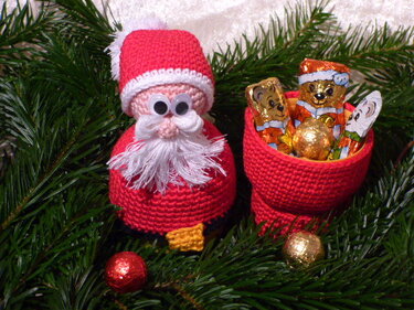 Roter gehäkelter Nikolaus mit weißem Bart neben offenem rotem Häkel-Stiefel voller Schokoladenfiguren auf Tannengrün