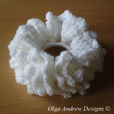 White crocheted ruffle scrunchie on a wooden surface