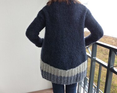 Rückenansicht: Person in langer dunkelblauer gestrickter Jacke mit hellgrauem Saum