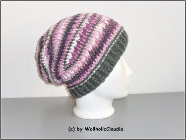 Gehäkelte Slouch-Mütze in Lila, Grau und Weiß mit dunkelgrauem Rippenbündchen auf weißem Schaufensterkopf.
