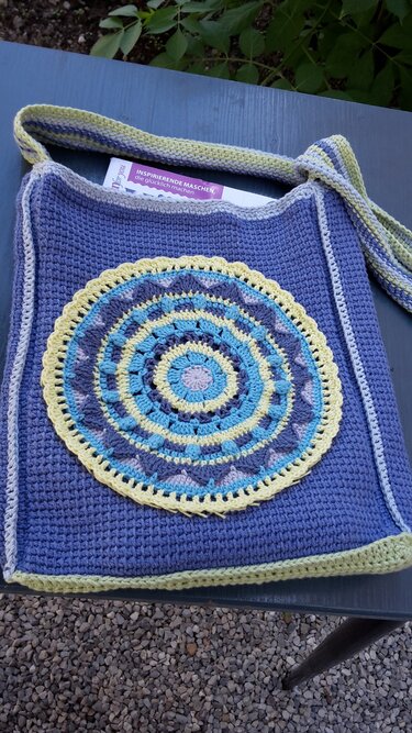 Gehäkelte lila Tasche mit rundem Mandala-Motiv in Gelb, Blau und Violett auf der Vorderseite
