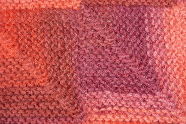 Nahaufnahme eines gestrickten Schals in orange-rosa Farbverlauf mit kraus-rechter Maschenstruktur