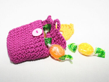 Magenta crocheted pouch with a pink button open to reveal wrapped candies.