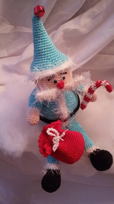 Gehäkelter hellblauer Weihnachtswichtel hält rot-weiße Zuckerstange und roten Sack