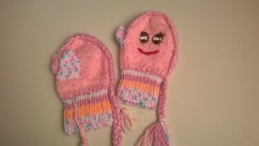 Gestrickte rosa Babyfäustlinge mit gesticktem Gesicht und geflochtenen Zöpfen