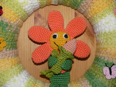 gehäkelter türkranz mit orangefarbener blume vor holzpaneel