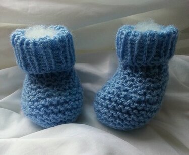 Hellblaue handgestrickte Babyschühchen mit geripptem Bündchen auf weißem Stoff