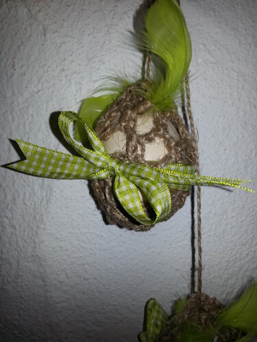 Hängendes Ei in gehäkelter Jutehülle mit grün kariertem Schleifenband und Feder