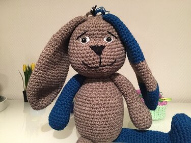 Gehäkelter Amigurumi-Hase in Braun mit blauen Akzenten an Ohr, Arm und Bein.