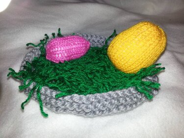 Gestricktes graues Osternest mit grünem Garn und zwei gestrickten Eiern in Rosa und Gelb