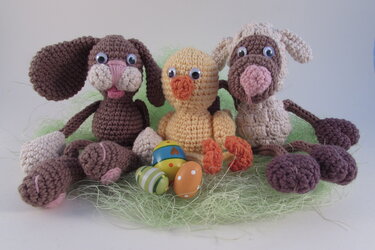Gehäkelter Hase, Lamm und Küken mit bunten Ostereiern im grünen Nest
